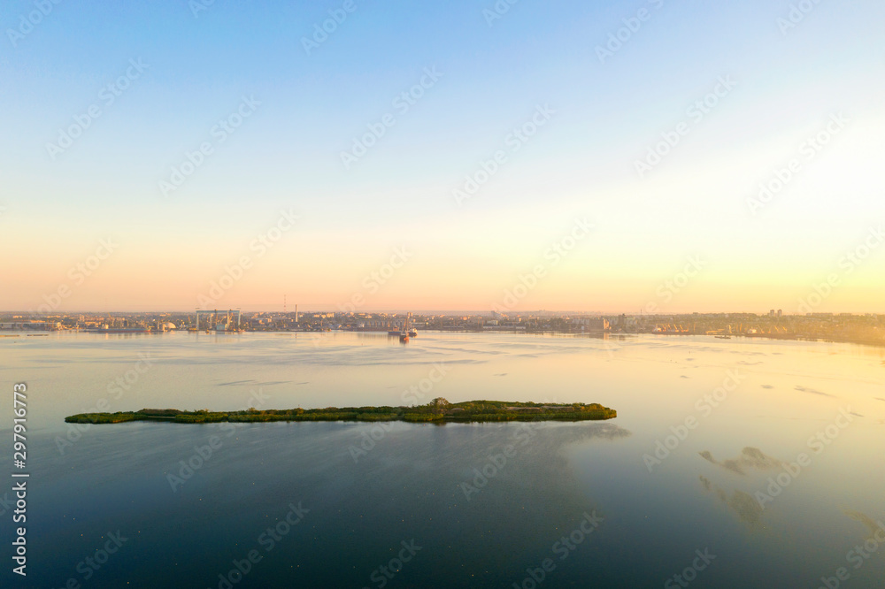 Dawn at the industrial city with a port and an island in the foreground. Drone photography