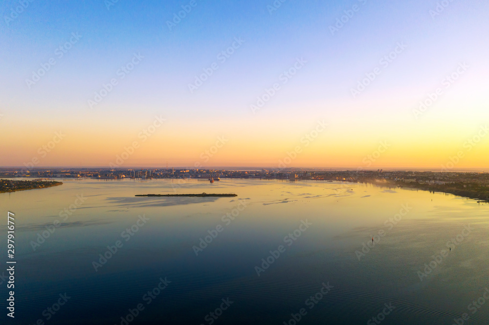 Dawn at the industrial city with a port and an island in the foreground. Drone photography