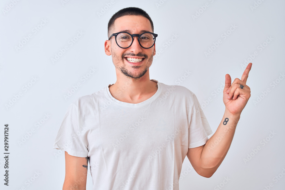 Young handsome man wearing glasses and standing over isolated background with a big smile on face, pointing with hand and finger to the side looking at the camera. Young handsome man wearing glasses and standing over isolated background with a big smile on face, pointing with hand and finger to the side looking at the camera.
