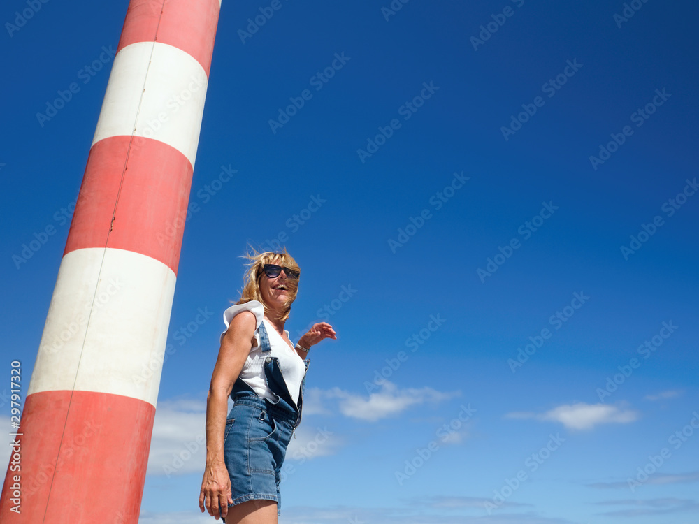   A young woman stands next to a part of a red and white striped lighthouse