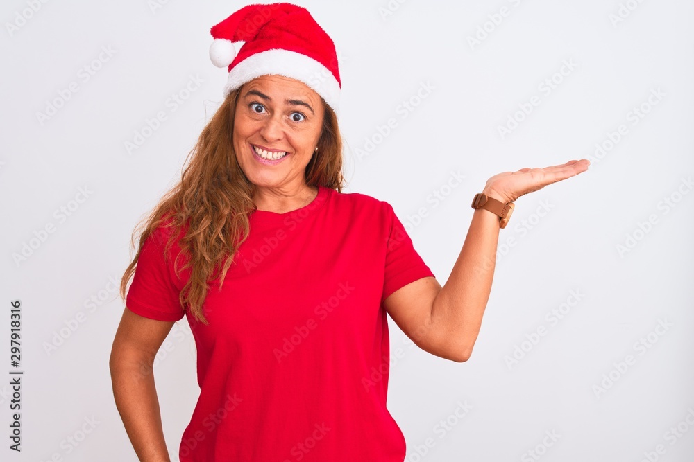 Middle age mature woman wearing christmas hat over isolated background smiling cheerful presenting and pointing with palm of hand looking at the camera. Middle age mature woman wearing christmas hat over isolated background smiling cheerful presenting and pointing with palm of hand looking at the camera.