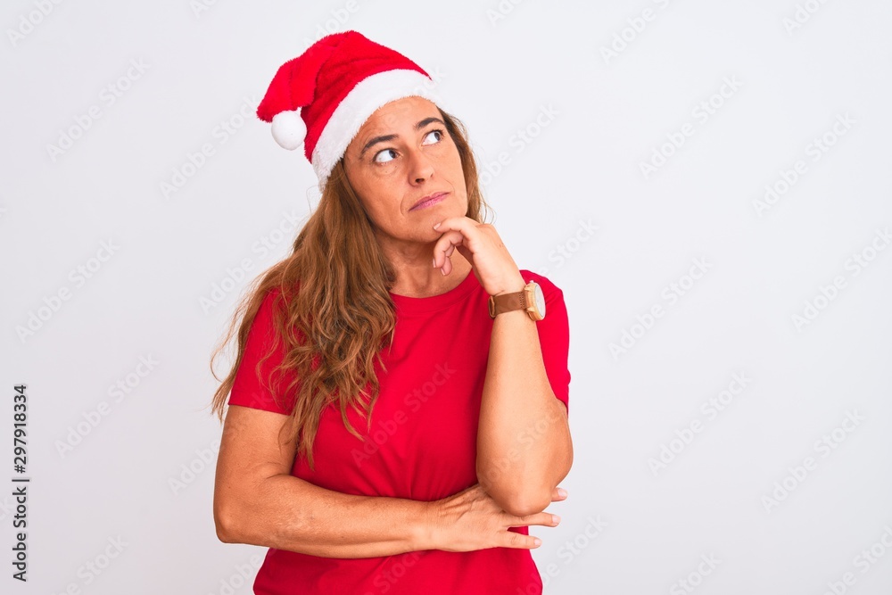 Middle age mature woman wearing christmas hat over isolated background with hand on chin thinking about question, pensive expression. Smiling with thoughtful face. Doubt concept. Middle age mature woman wearing christmas hat over isolated background with hand on chin thinking about question, pensive expression. Smiling with thoughtful face. Doubt concept.