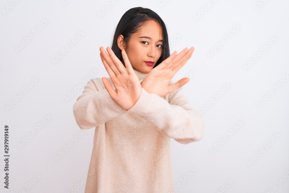 Young chinese woman wearing turtleneck sweater standing over isolated white background Rejection expression crossing arms and palms doing negative sign, angry face Young chinese woman wearing turtleneck sweater standing over isolated white background Rejection expression crossing arms and palms doing negative sign, angry face
