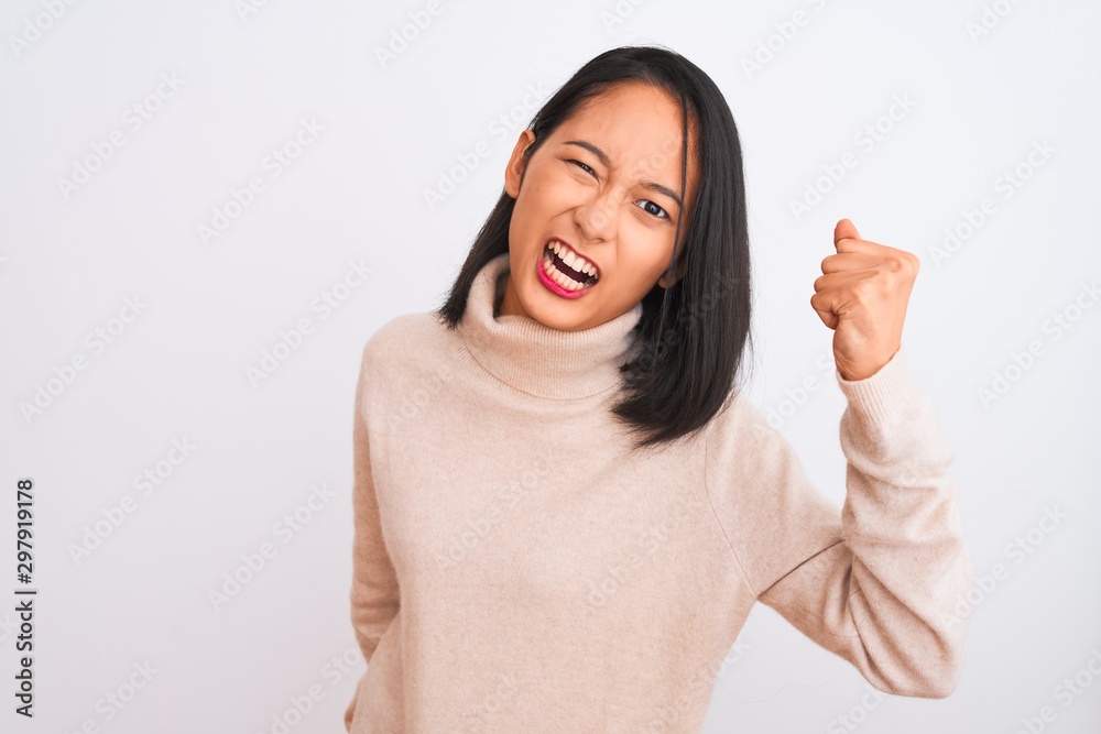 Young chinese woman wearing turtleneck sweater standing over isolated white background angry and mad raising fist frustrated and furious while shouting with anger. Rage and aggressive concept. Young chinese woman wearing turtleneck sweater standing over isolated white background angry and mad raising fist frustrated and furious while shouting with anger. Rage and aggressive concept.