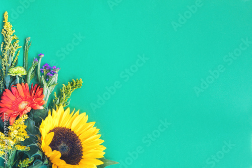Corner border of different fresh bright colorful summer flowers lying on trendy mint background. Flat lay style. Copy space.