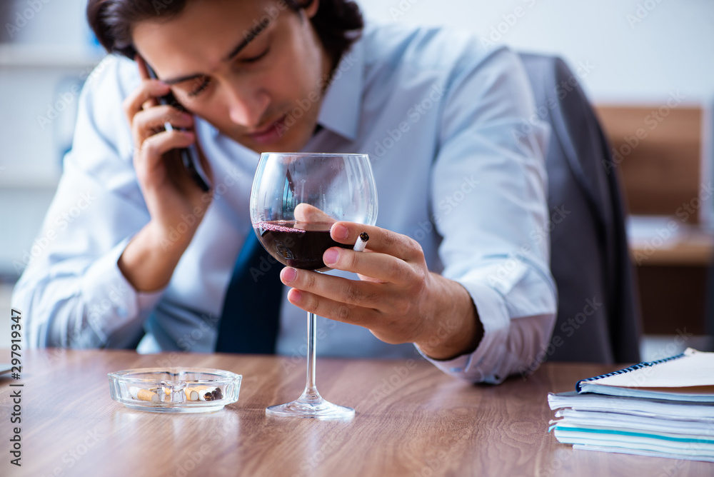 Male employee drinking alcohol and smoking cigarettes at workpla Male employee drinking alcohol and smoking cigarettes at workpla