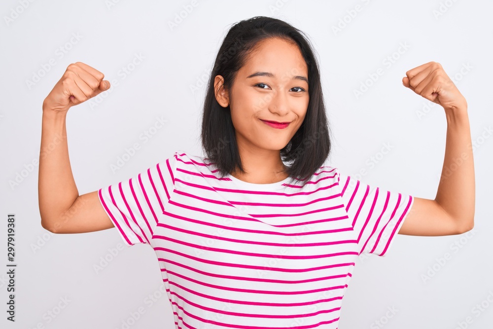 Young chinese woman wearing striped t-shirt standing over isolated white background showing arms muscles smiling proud. Fitness concept. Young chinese woman wearing striped t-shirt standing over isolated white background showing arms muscles smiling proud. Fitness concept.