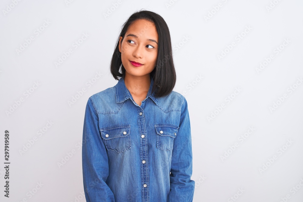 Young beautiful chinese woman wearing denim shirt standing over isolated white background smiling looking to the side and staring away thinking. Young beautiful chinese woman wearing denim shirt standing over isolated white background smiling looking to the side and staring away thinking.