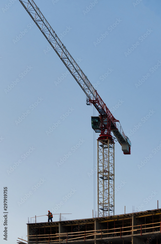 Landscape construction of a large building. There is a tall construction crane and building frame. A small human figure does the work in the lower left corner of the frame. Background. Decoration.