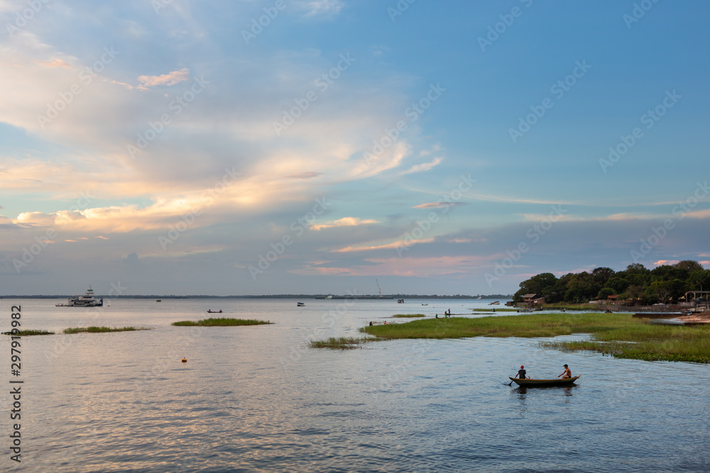 Silhouette of two men fishing in small boat on Amazon river at dusk in day with blue sky and clouds. Travel, peace, vacation, mindfulness, environment, tranquility and trip concept.