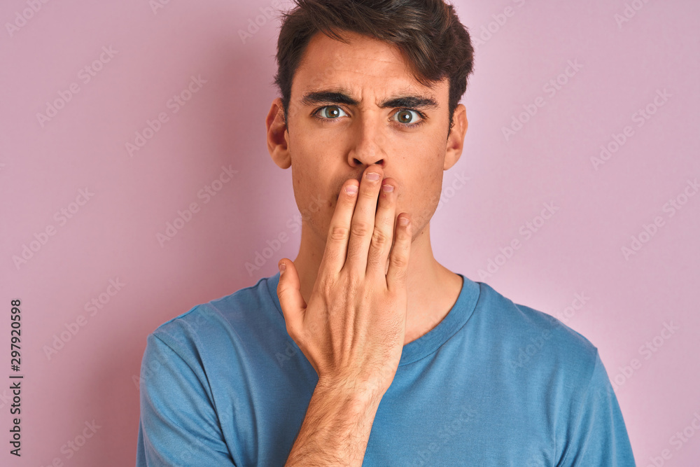 Teenager boy wearing casual t-shirt standing over blue isolated background cover mouth with hand shocked with shame for mistake, expression of fear, scared in silence, secret concept Teenager boy wearing casual t-shirt standing over blue isolated background cover mouth with hand shocked with shame for mistake, expression of fear, scared in silence, secret concept