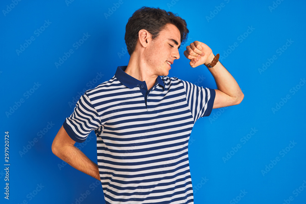 Teenager boy wearing casual t-shirt standing over blue isolated background stretching back, tired and relaxed, sleepy and yawning for early morning Teenager boy wearing casual t-shirt standing over blue isolated background stretching back, tired and relaxed, sleepy and yawning for early morning