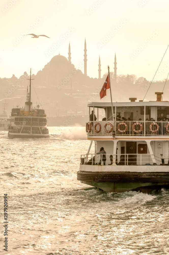 Fototapeta premium Muslim architecture and water transport in Turkey - Beautiful View touristic landmarks from sea voyage on Bosphorus. Cityscape of Istanbul at sunset - old mosque and turkish steamboats, view on Golden
