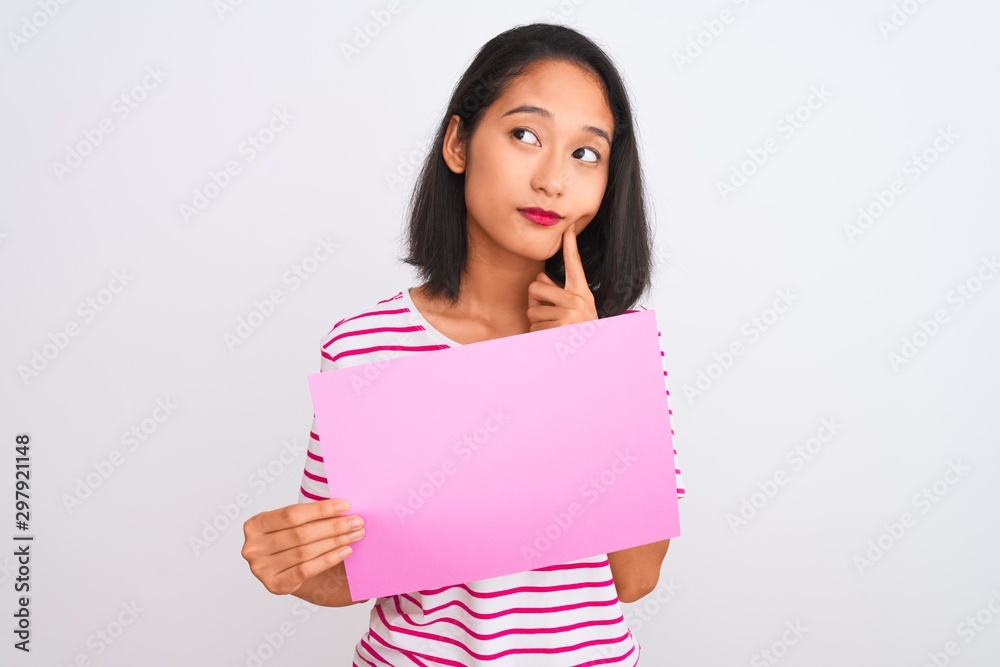 Young beautiful chinese woman holding banner standing over isolated white background serious face thinking about question, very confused idea Young beautiful chinese woman holding banner standing over isolated white background serious face thinking about question, very confused idea