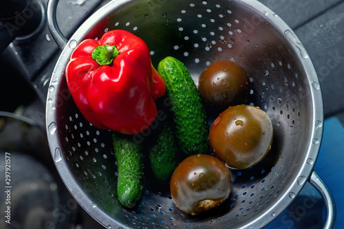 Fresh tasty organic wet vegetables in stainless steel colander after washing with water in sink at home kitchen. Healthe vegan food diet. High-fibers salad ingridients. Pepper, cucumber and tomato photo