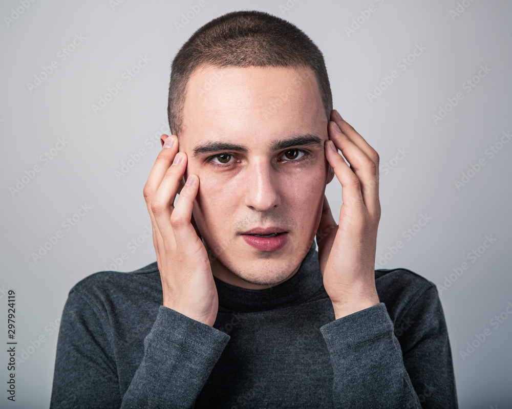Feared unhappy crying man with shocked face with headache holding the head. Closeup studio portrait on grey background. Negative problem concept Feared unhappy crying man with shocked face with headache holding the head. Closeup studio portrait on grey background. Negative problem concept
