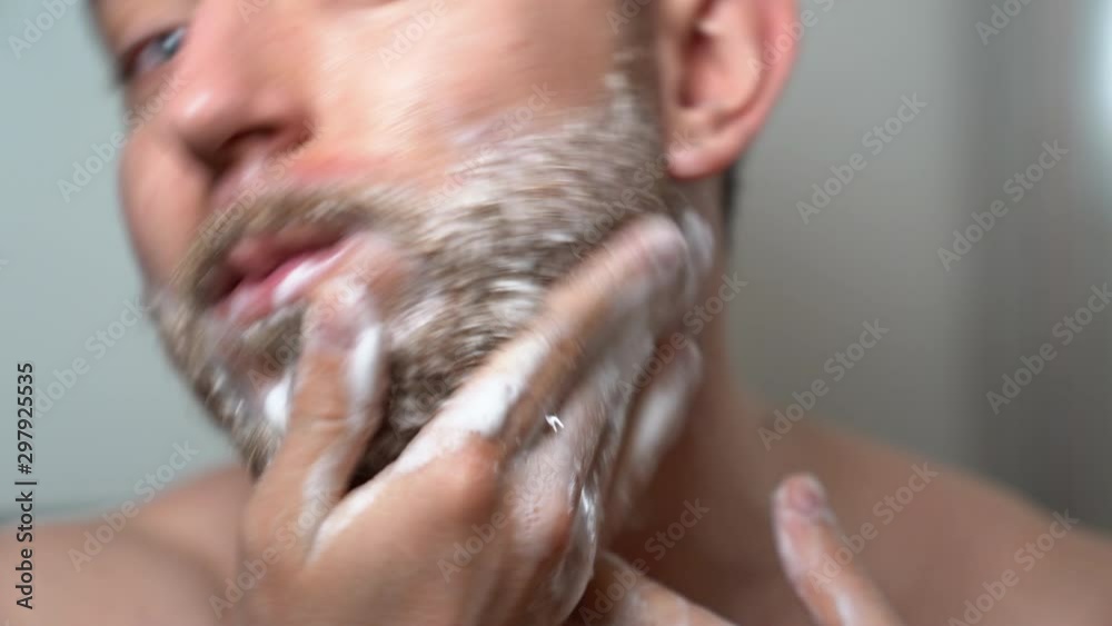 Professional barber man washing his unshaved beard before cutting with electric trimmer. Soaping beard, shampoo foam and special technics in shaving beard at home. Skincare and beard grooming concept