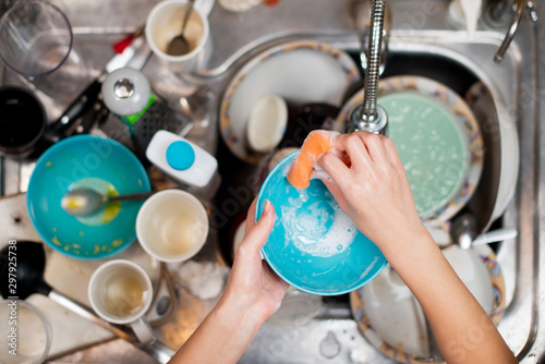 girl washes a dirty plate on the background of the sink with dirty dishes