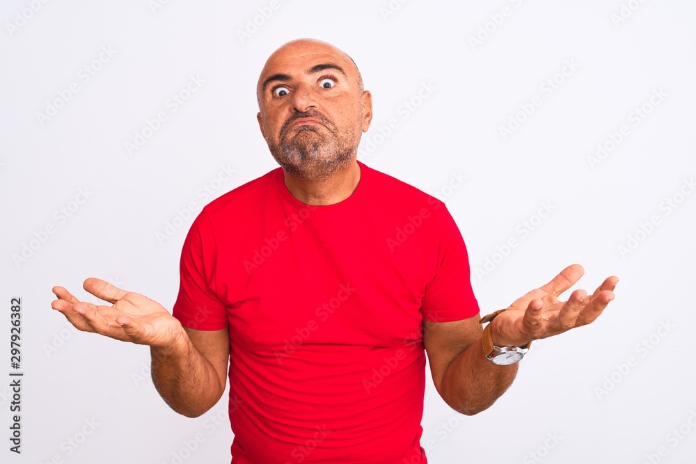 Fototapeta premium Middle age handsome man wearing red casual t-shirt standing over isolated white background clueless and confused expression with arms and hands raised. Doubt concept.