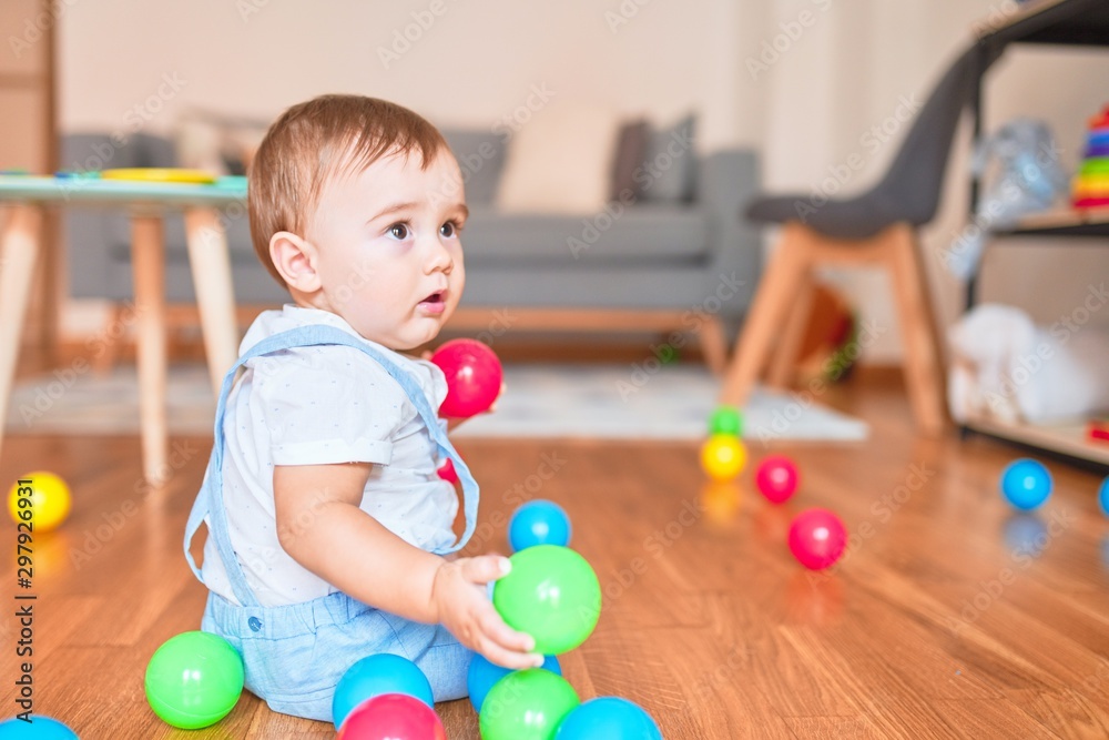 Beautiful toddler sitting on the floor playing with small colorful balls at kindergarten Beautiful toddler sitting on the floor playing with small colorful balls at kindergarten