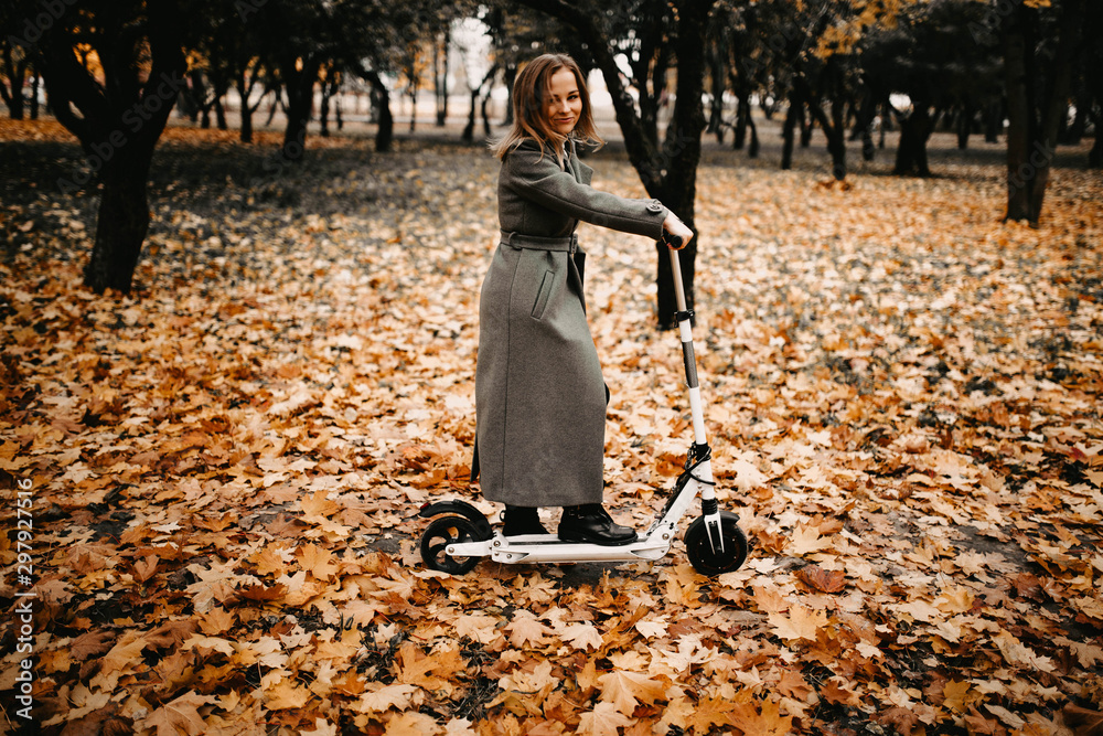 Woman in a coat in autumn on an electric scooter in an autumn park. Riding  on electric vehicles in cold weather. Stock Photo | Adobe Stock