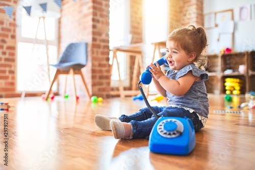 Beautiful toddler sitting on the floor playing with vintage phone at kindergarten photo