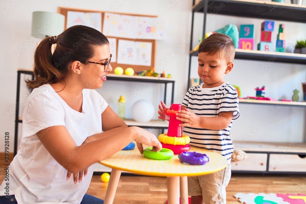 Beautiful teacher and toddler boy building pyramid with hoops bolcks at kindergarten
