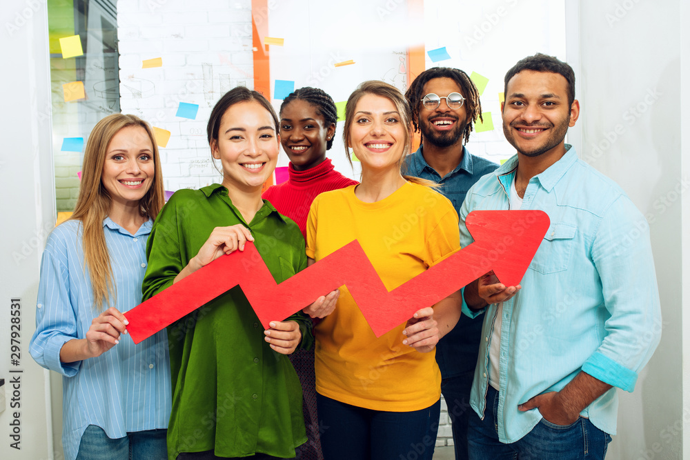 Young happy and colorful business team hold a red statistical arrow. Concept of growing, succesful and profit Young happy and colorful business team hold a red statistical arrow. Concept of growing, succesful and profit