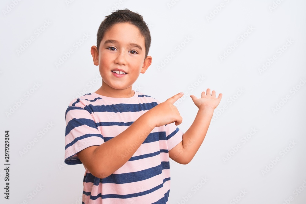 Beautiful kid boy wearing casual striped t-shirt standing over isolated white background amazed and smiling to the camera while presenting with hand and pointing with finger. Beautiful kid boy wearing casual striped t-shirt standing over isolated white background amazed and smiling to the camera while presenting with hand and pointing with finger.