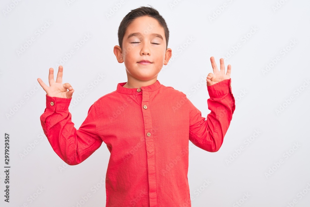 Beautiful kid boy wearing elegant red shirt standing over isolated white background relax and smiling with eyes closed doing meditation gesture with fingers. Yoga concept.