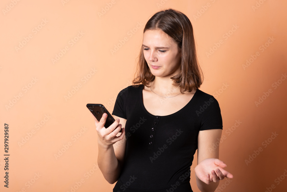 Girl shows discontent with a smartphone, on a light orange background. Girl shows discontent with a smartphone, on a light orange background.