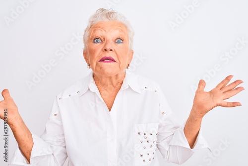 Senior grey-haired woman wearing elegant shirt standing over isolated white background clueless and confused expression with arms and hands raised. Doubt concept.