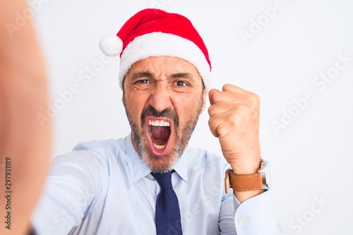 Middle age businessman wearing christmas hat make selfie over isolated white background annoyed and frustrated shouting with anger, crazy and yelling with raised hand, anger concept