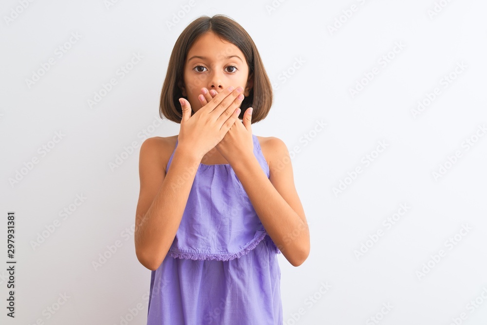Young beautiful child girl wearing purple casual dress standing over isolated white background shocked covering mouth with hands for mistake. Secret concept. Young beautiful child girl wearing purple casual dress standing over isolated white background shocked covering mouth with hands for mistake. Secret concept.