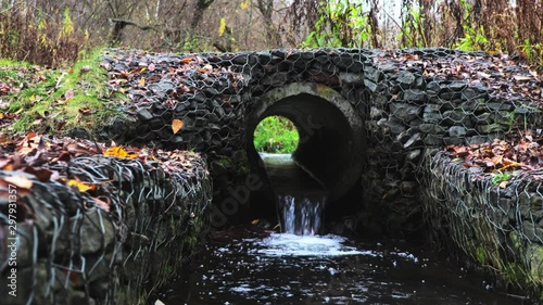 Small brook flowing through concrete pipe in the park