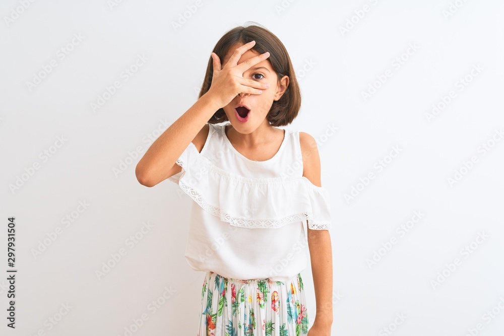 Young beautiful child girl wearing casual dress standing over isolated white background peeking in shock covering face and eyes with hand, looking through fingers with embarrassed expression. Young beautiful child girl wearing casual dress standing over isolated white background peeking in shock covering face and eyes with hand, looking through fingers with embarrassed expression.