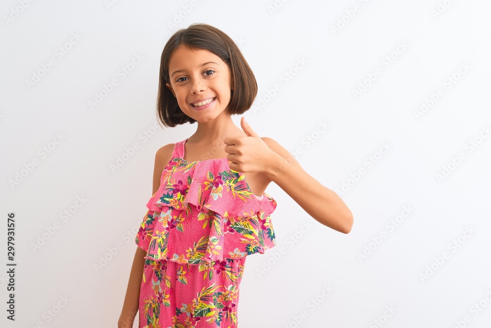 Young beautiful child girl wearing pink floral dress standing over isolated white background doing happy thumbs up gesture with hand. Approving expression looking at the camera showing success. Young beautiful child girl wearing pink floral dress standing over isolated white background doing happy thumbs up gesture with hand. Approving expression looking at the camera showing success.
