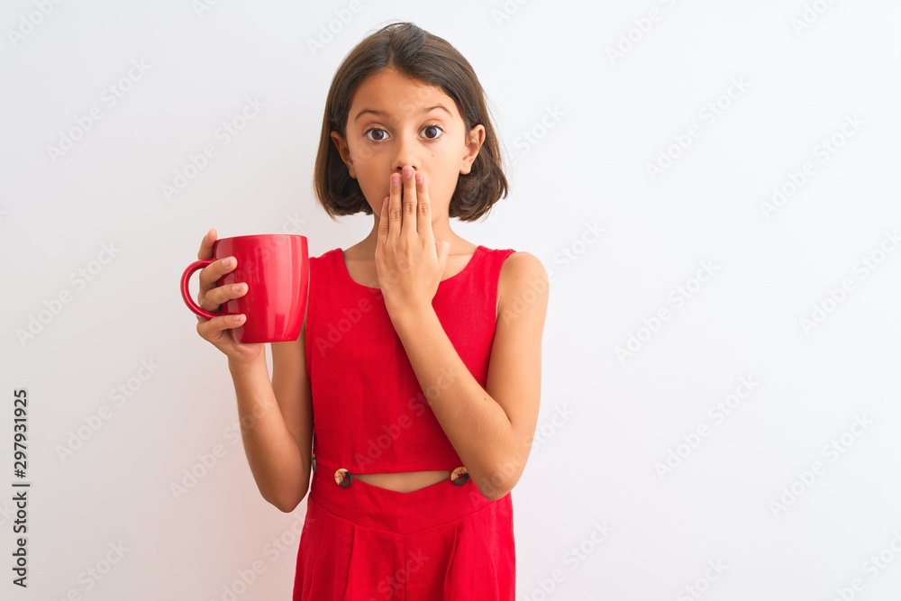 Beautiful child girl holding red cup of tea standing over isolated white background cover mouth with hand shocked with shame for mistake, expression of fear, scared in silence, secret concept Beautiful child girl holding red cup of tea standing over isolated white background cover mouth with hand shocked with shame for mistake, expression of fear, scared in silence, secret concept