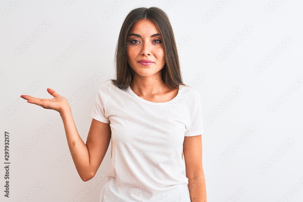 Young beautiful woman wearing casual t-shirt standing over isolated white background smiling cheerful presenting and pointing with palm of hand looking at the camera. Young beautiful woman wearing casual t-shirt standing over isolated white background smiling cheerful presenting and pointing with palm of hand looking at the camera.