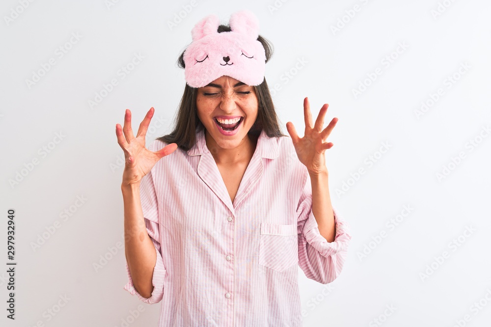Young beautiful woman wearing sleep mask and pajama over isolated white background celebrating mad and crazy for success with arms raised and closed eyes screaming excited. Winner concept Young beautiful woman wearing sleep mask and pajama over isolated white background celebrating mad and crazy for success with arms raised and closed eyes screaming excited. Winner concept