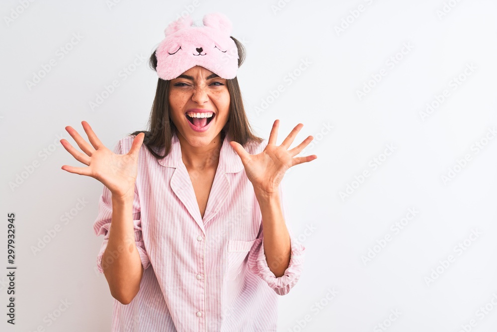Young beautiful woman wearing sleep mask and pajama over isolated white background celebrating crazy and amazed for success with arms raised and open eyes screaming excited. Winner concept Young beautiful woman wearing sleep mask and pajama over isolated white background celebrating crazy and amazed for success with arms raised and open eyes screaming excited. Winner concept