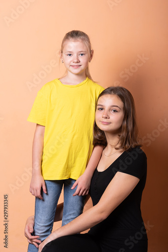 Two girls, sisters, on a light orange background.