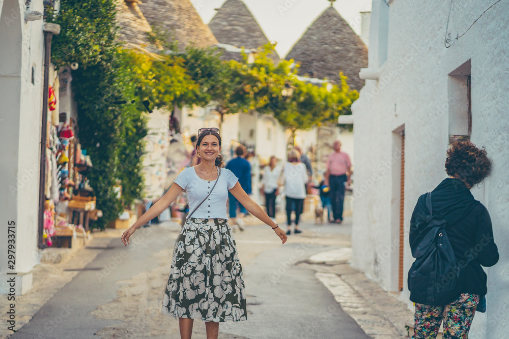 happy tourist girl woman take selfie photo in Alberobello town, Apulia, southern Italy. The town of alberobello is famous for the typical white trulli houses. Unidentified tourits walking in the city happy tourist girl woman take selfie photo in Alberobello town, Apulia, southern Italy. The town of alberobello is famous for the typical white trulli houses. Unidentified tourits walking in the city