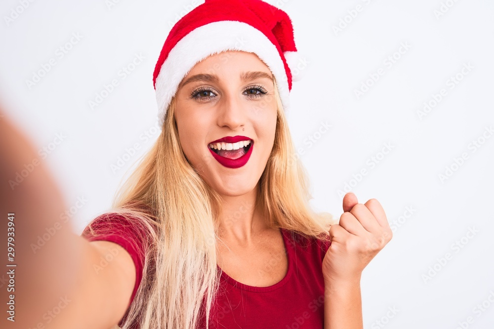 Woman wearing Christmas Santa hat make selfie by camera over isolated white background screaming proud and celebrating victory and success very excited, cheering emotion Woman wearing Christmas Santa hat make selfie by camera over isolated white background screaming proud and celebrating victory and success very excited, cheering emotion
