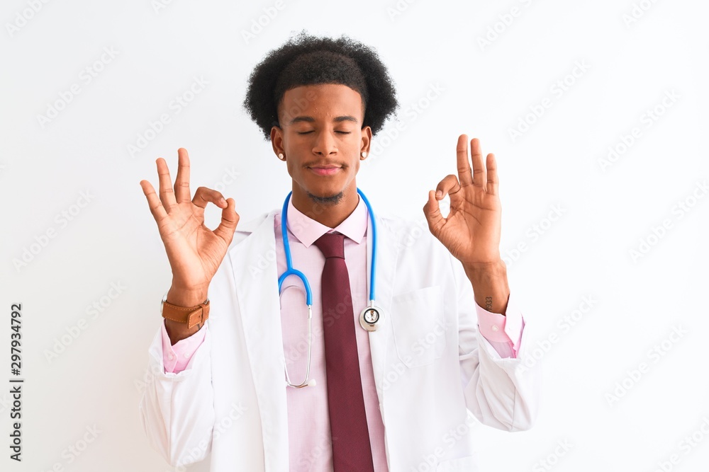 Young african american doctor man wearing sthetoscope over isolated white background relax and smiling with eyes closed doing meditation gesture with fingers. Yoga concept. Young african american doctor man wearing sthetoscope over isolated white background relax and smiling with eyes closed doing meditation gesture with fingers. Yoga concept.
