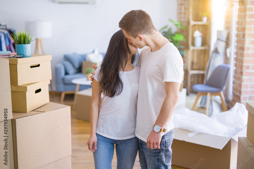 Young beautiful couple standing at new home around cardboard boxes Young beautiful couple standing at new home around cardboard boxes