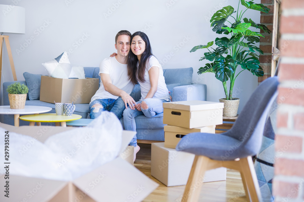 Young beautiful couple sitting on the sofa drinking coffee at new home around cardboard boxes