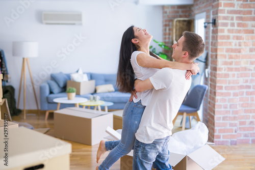 Young beautiful couple hugging at new home around cardboard boxes