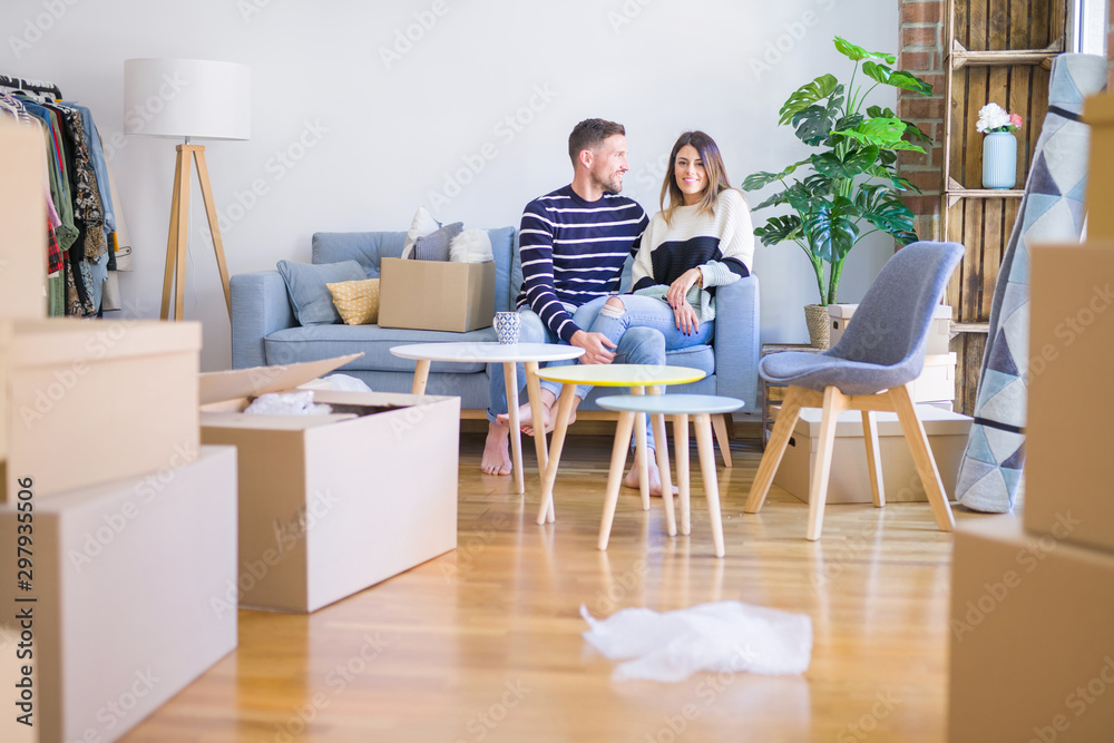 Young beautiful couple sitting on the sofa drinking cup of coffee at new home around cardboard boxes Young beautiful couple sitting on the sofa drinking cup of coffee at new home around cardboard boxes