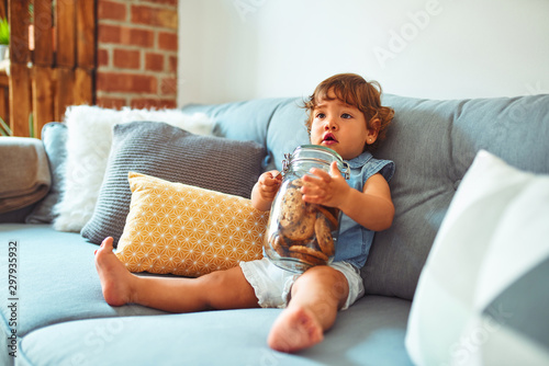 Billede på lærred Beautiful toddler child girl holding jar of cookies sitting on the sofa